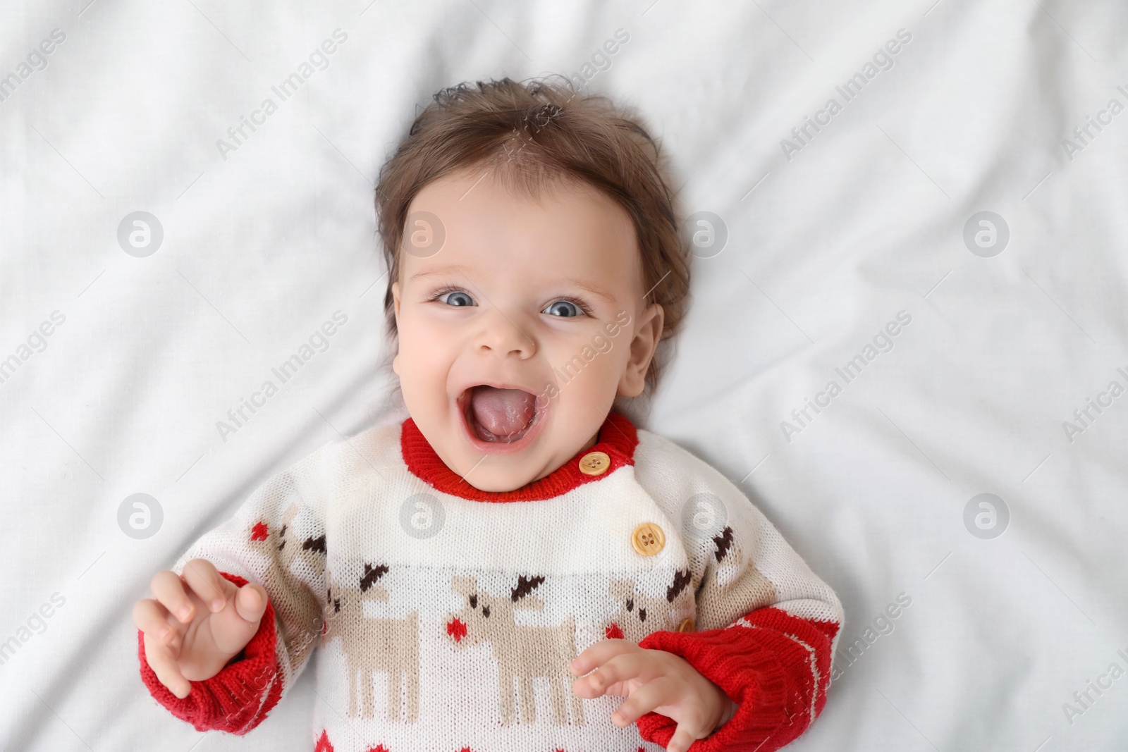 Photo of Cute little baby in Christmas sweater on soft bed, top view. Space for text