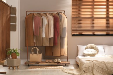 Photo of Garment bags with clothes hanging on rack in bedroom