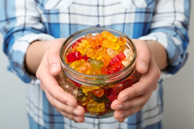 Photo of Woman holding jar of colorful jelly bears on light background, closeup