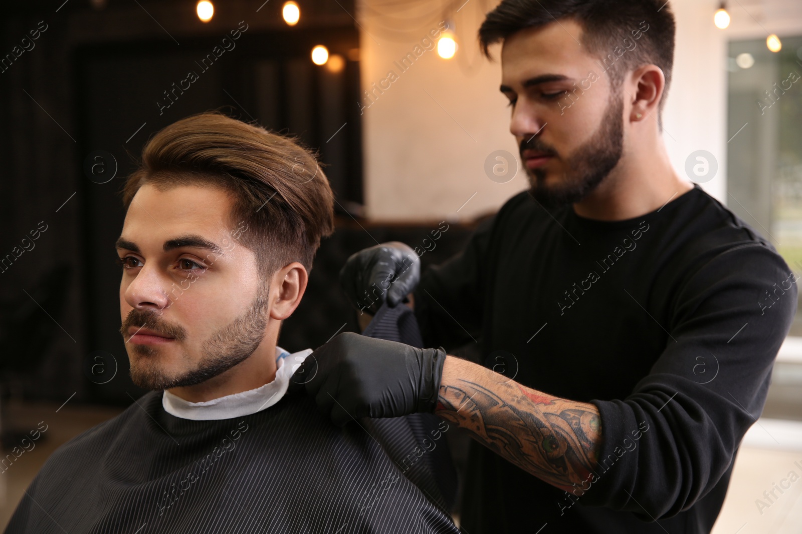 Photo of Professional hairdresser preparing client for shaving at barbershop