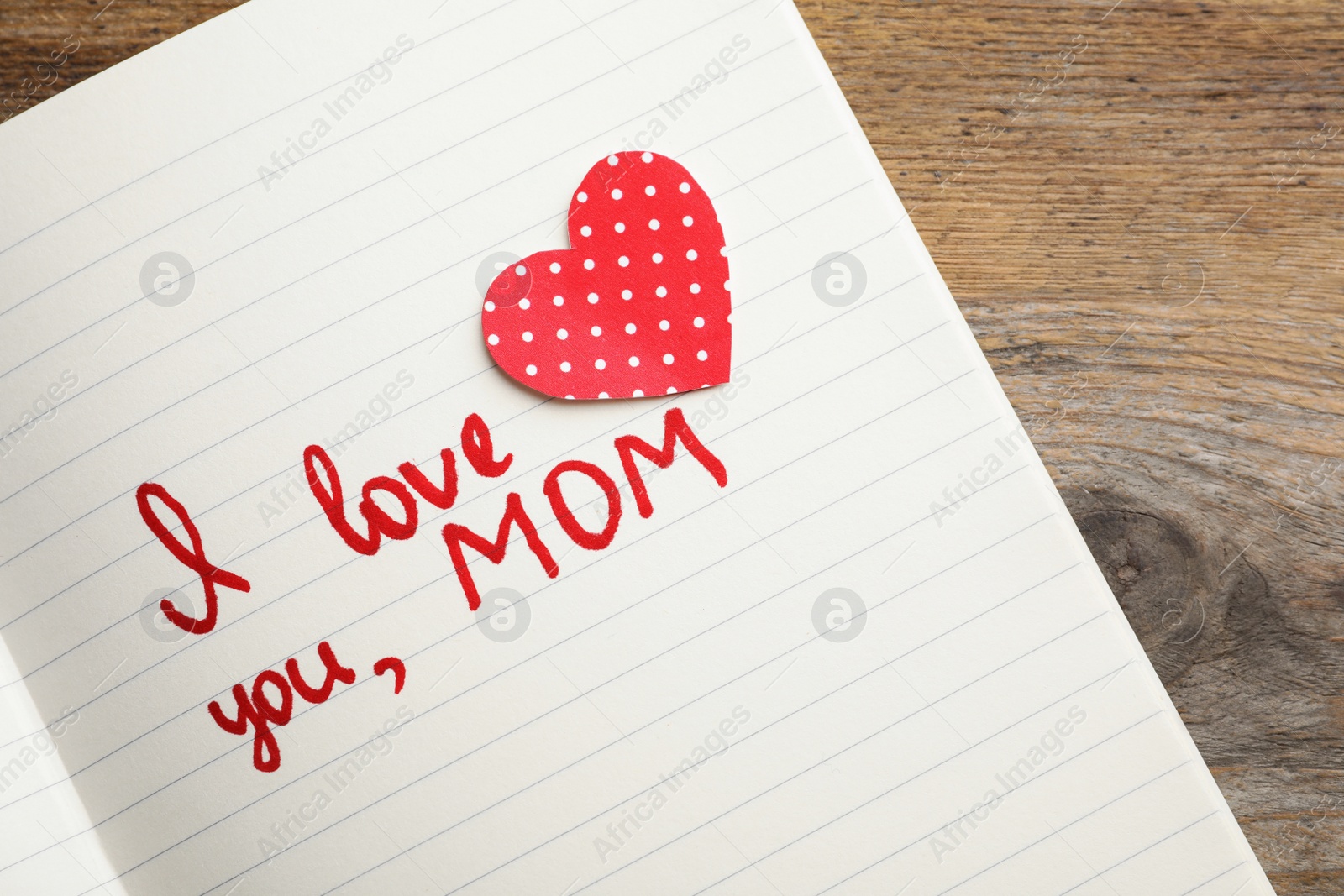 Photo of Notebook with words I LOVE YOU MOM and paper heart on wooden table, top view