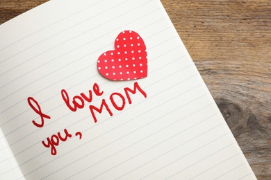 Notebook with words I LOVE YOU MOM and paper heart on wooden table, top view