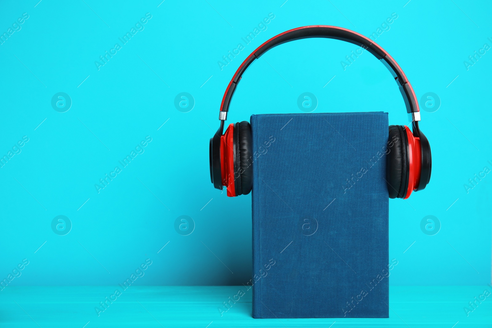 Photo of Book and modern headphones on light blue wooden table. Space for text