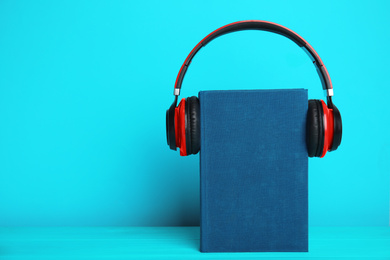 Book and modern headphones on light blue wooden table. Space for text