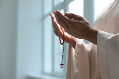 Muslim woman with misbaha praying indoors, closeup. Space for text