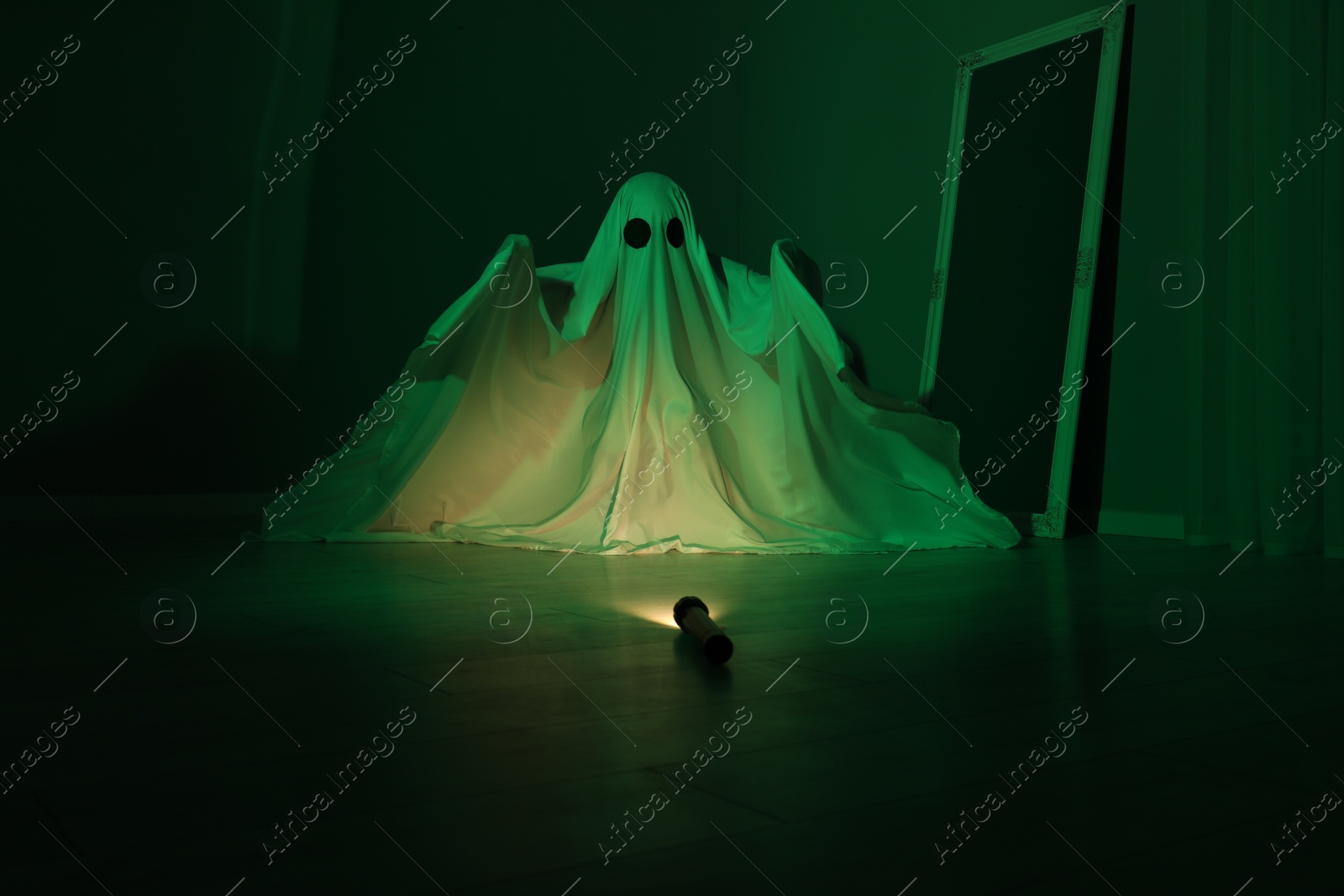 Photo of Creepy ghost. Woman covered with sheet in green light