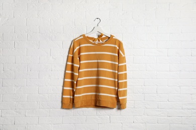 Hanger with stylish sweater on brick wall