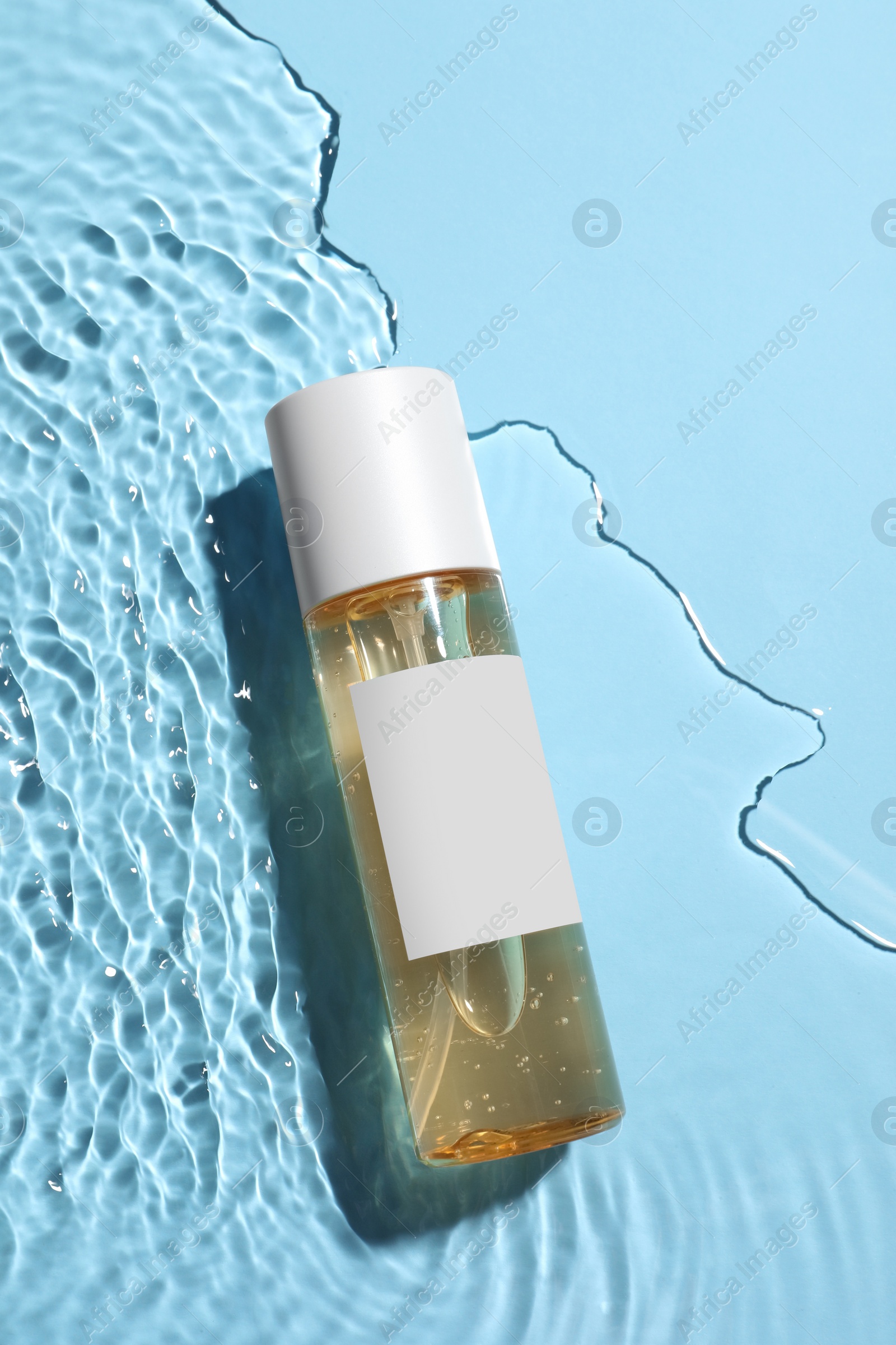 Photo of Bottle of cosmetic oil in water on light blue background, top view