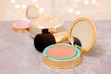 Photo of Face bronzer and makeup brush on grey textured table against blurred lights, closeup