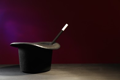 Photo of Magician's hat and wand on black wooden table against dark background, space for text