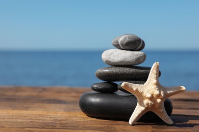 Photo of Stack of stones and starfish on wooden pier near sea, space for text Zen concept