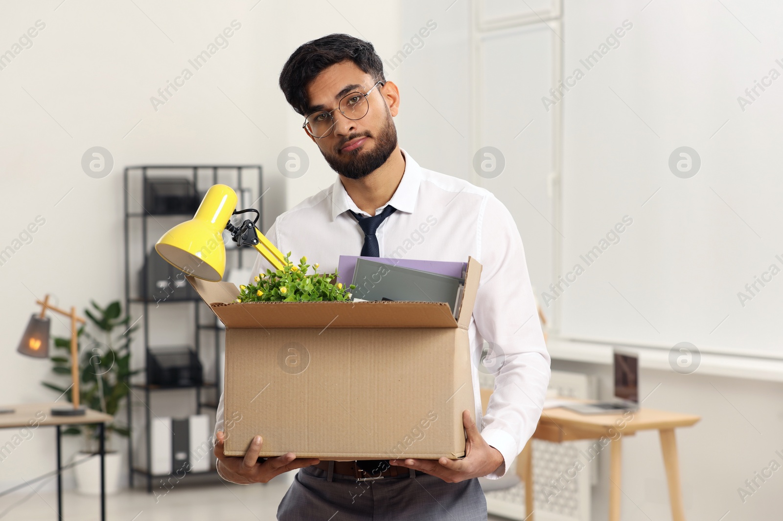 Photo of Unemployment problem. Frustrated man with box of personal belongings in office