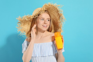 Beautiful young woman in straw hat with sun protection cream on light blue background