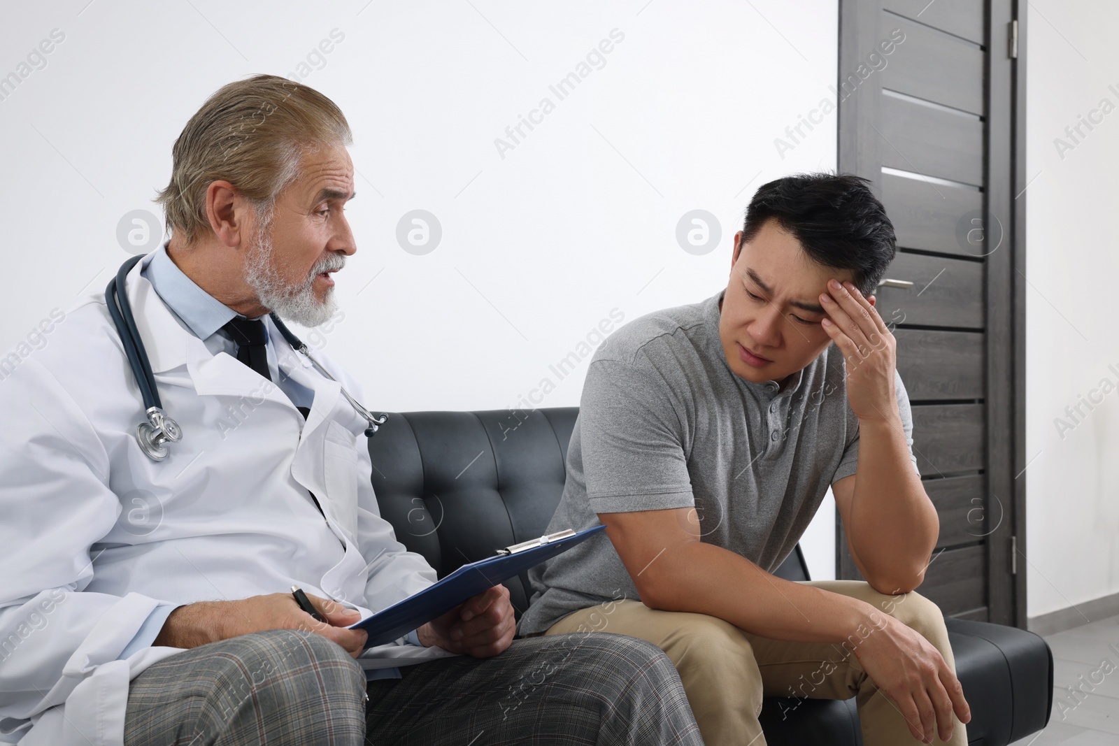 Photo of Senior doctor with clipboard consulting patient in clinic