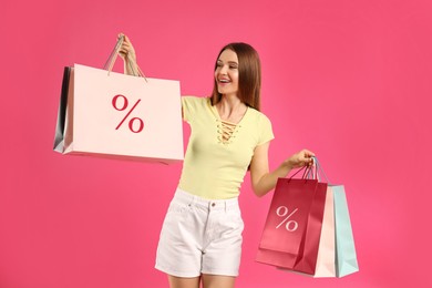 Image of Discount, sale, offer. Woman holding paper bags with percent signs against pink background