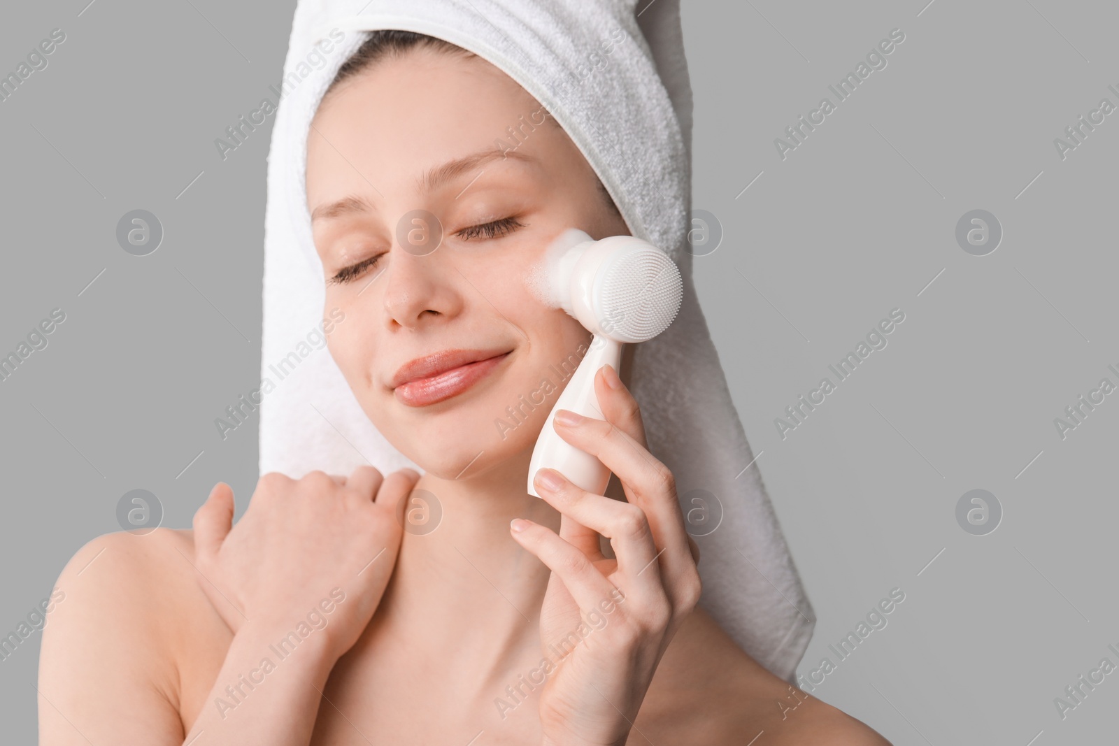 Photo of Young woman washing face with brush and cleansing foam on grey background. Space for text