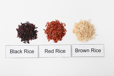 Photo of Different types of uncooked rice and cards on white background, top view