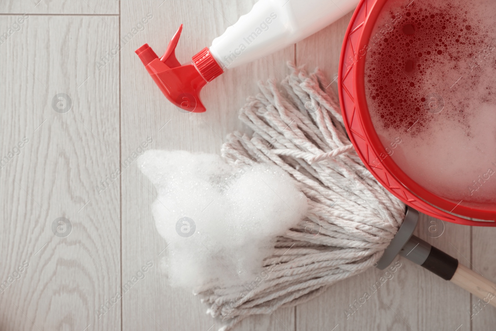 Photo of Bucket, mop and bottle of cleaning product on floor indoors, flat lay