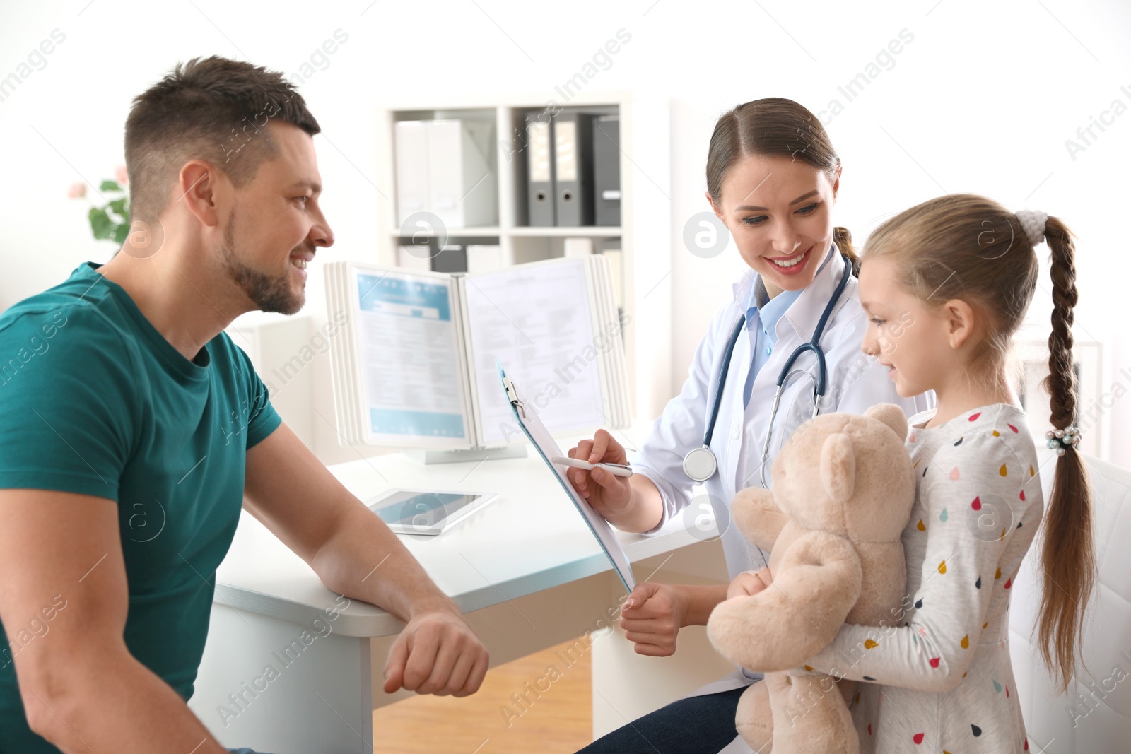 Photo of Father and daughter visiting pediatrician. Doctor working with little patient in hospital