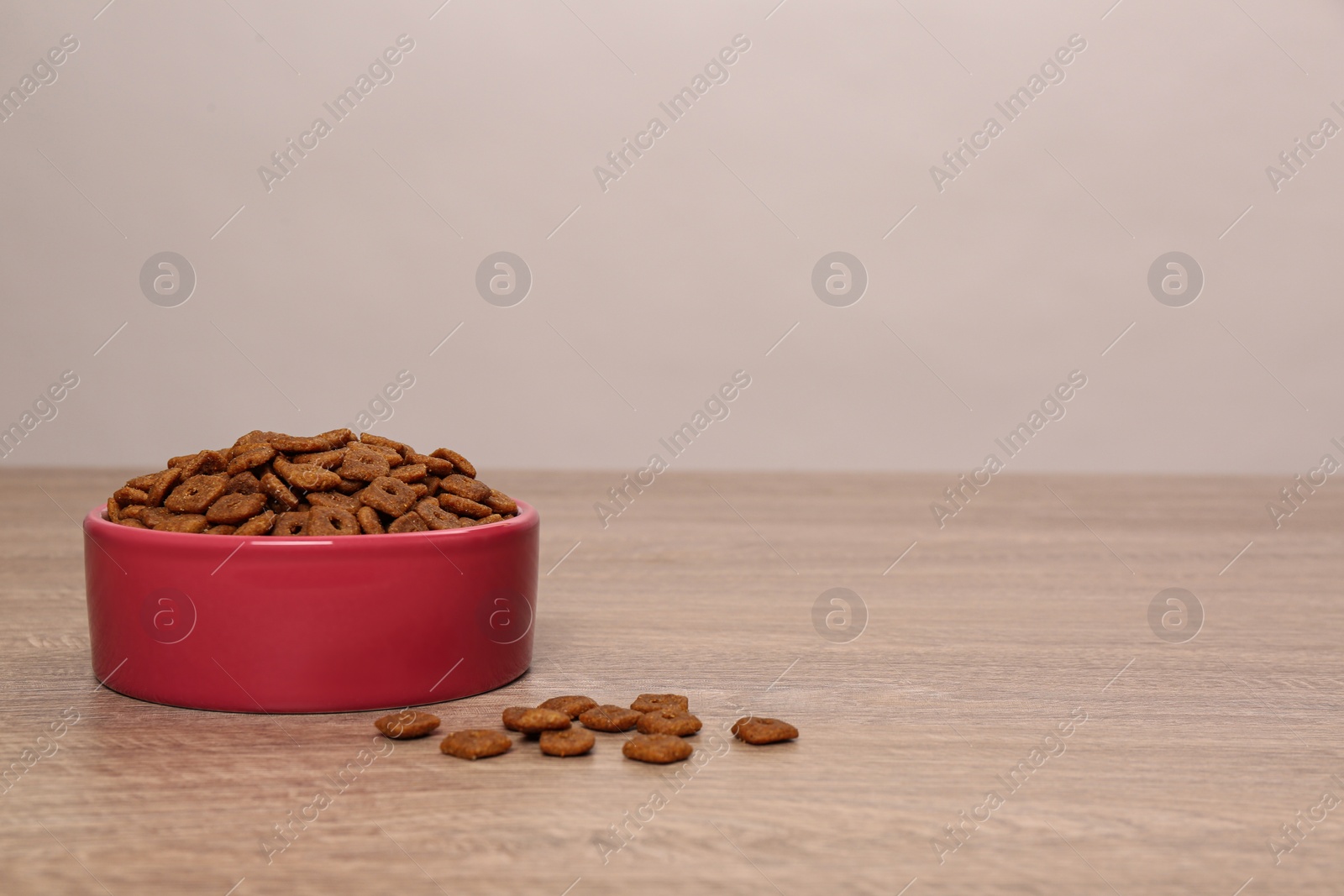 Photo of Dry food in pet bowl on wooden surface, space for text