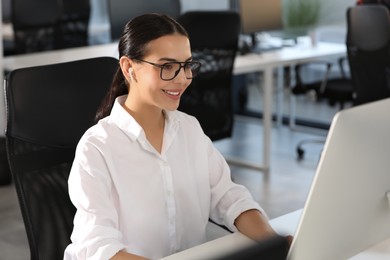 Happy woman with earphones using modern computer at desk in office
