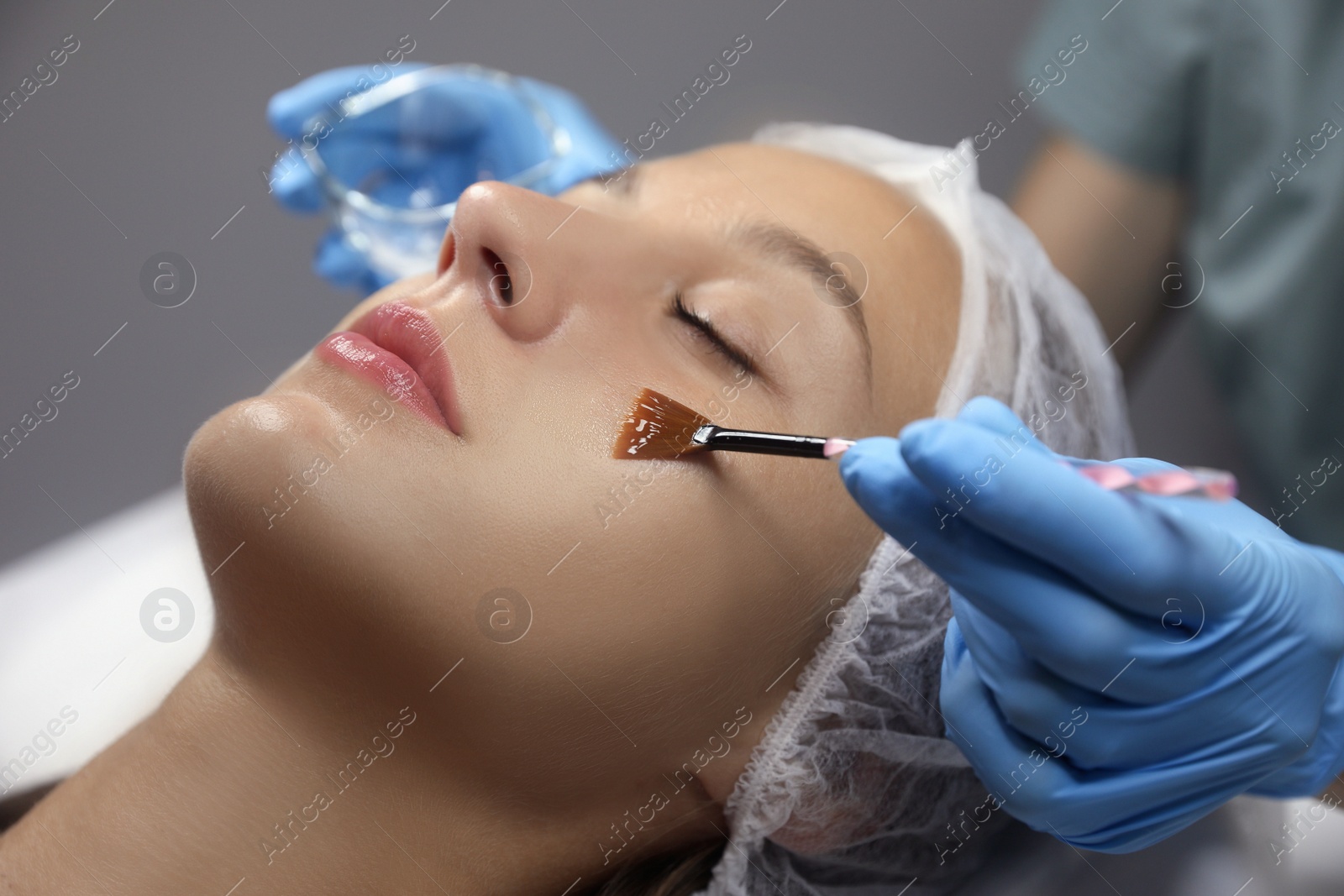 Photo of Cosmetologist applying chemical peel product on client's face in salon