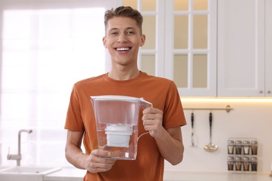 Photo of Happy man with water filter jug in kitchen