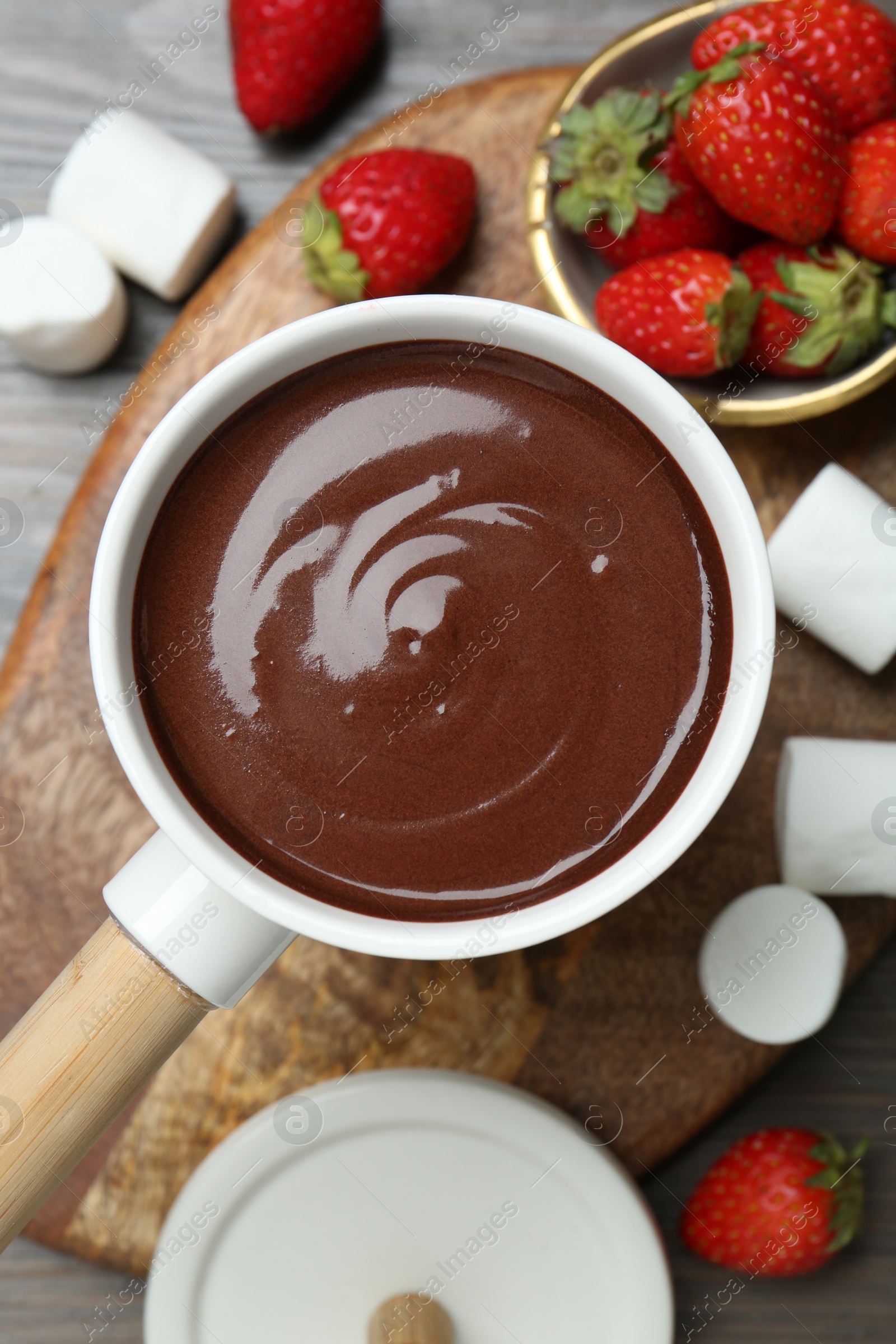 Photo of Fondue pot with melted chocolate, sweet marshmallows and strawberries on wooden table, flat lay