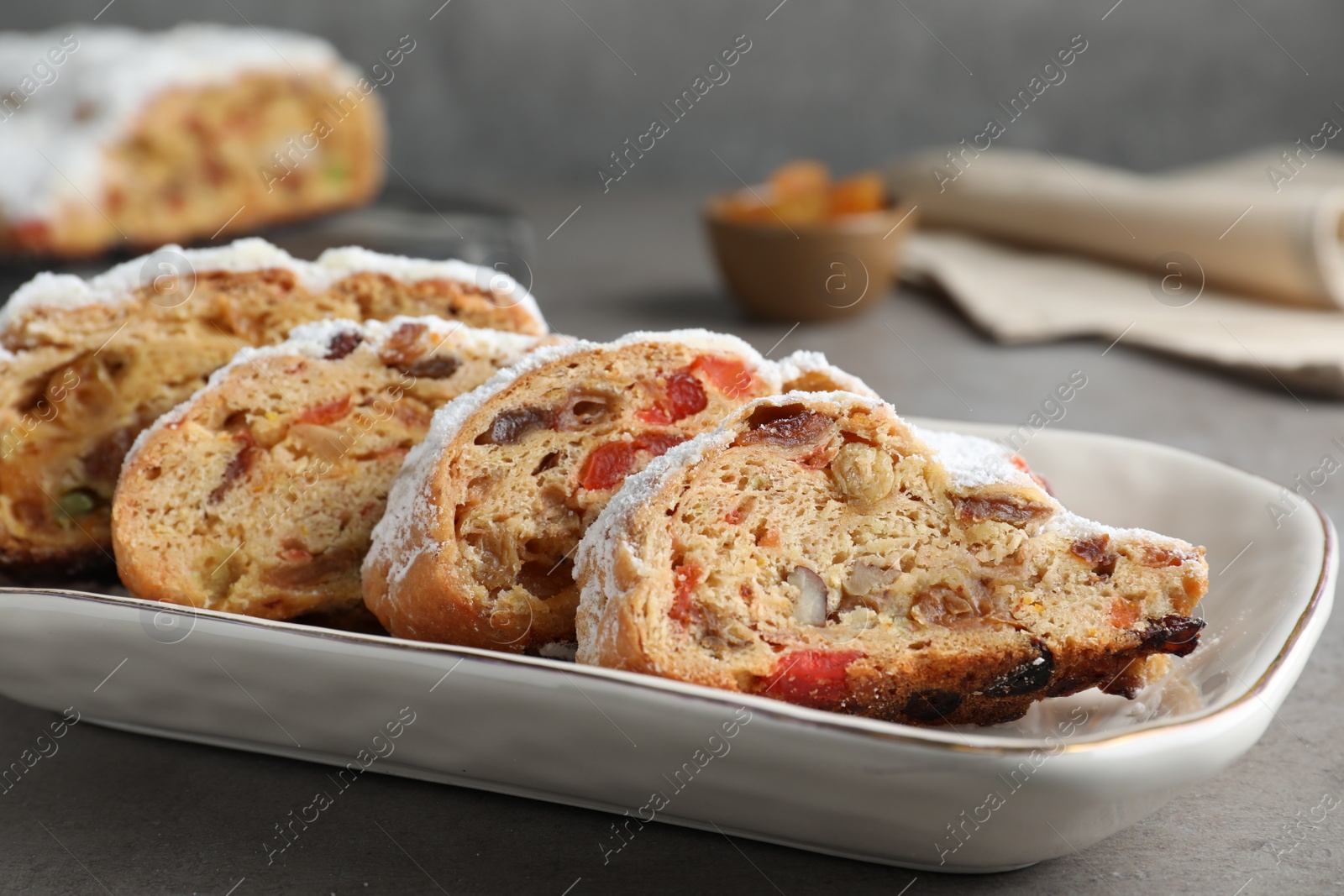 Photo of Traditional Christmas Stollen with icing sugar on grey table, closeup