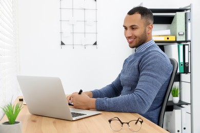 Photo of Happy young intern working with laptop at table in modern office