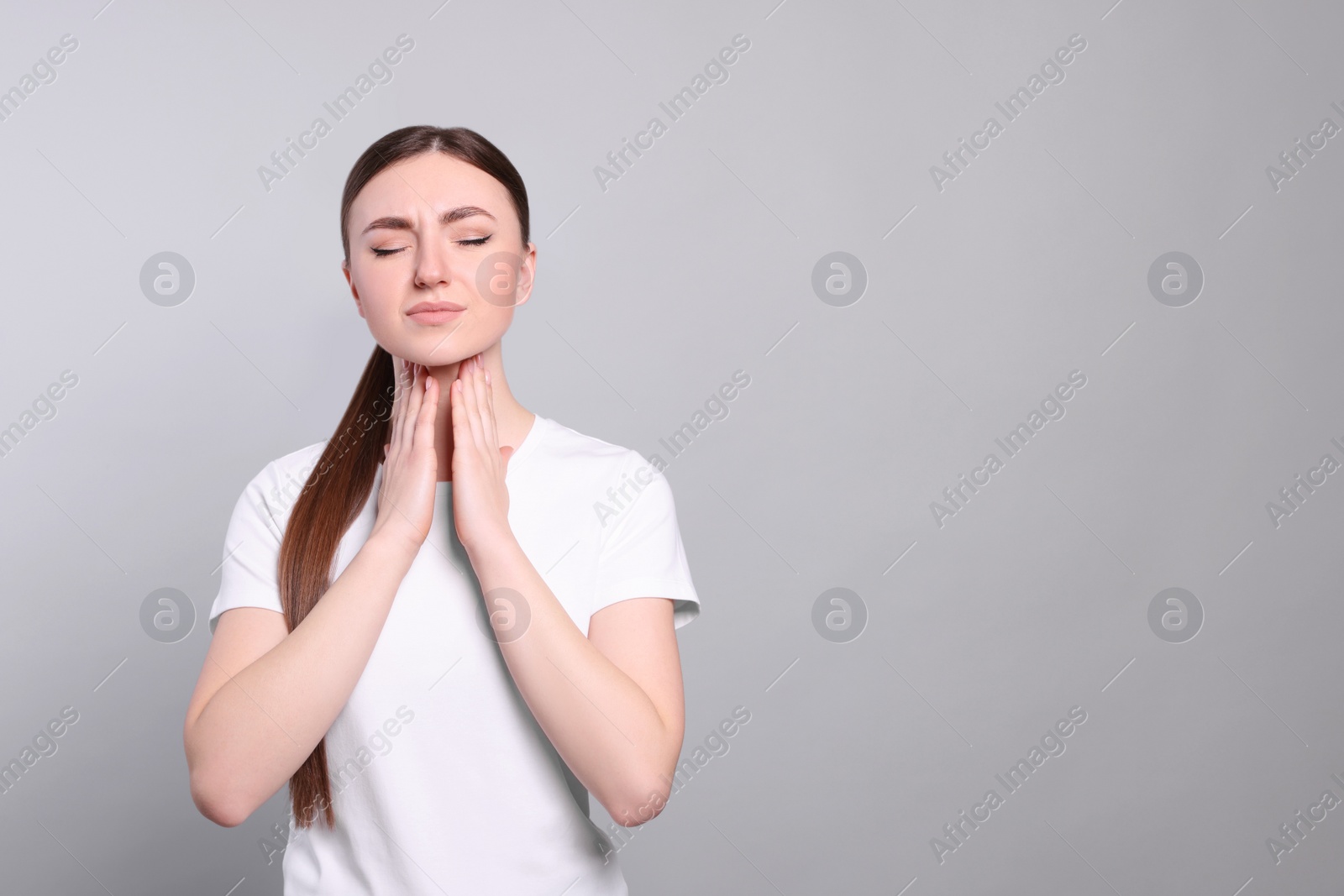 Photo of Young woman with sore throat on light grey background. Space for text