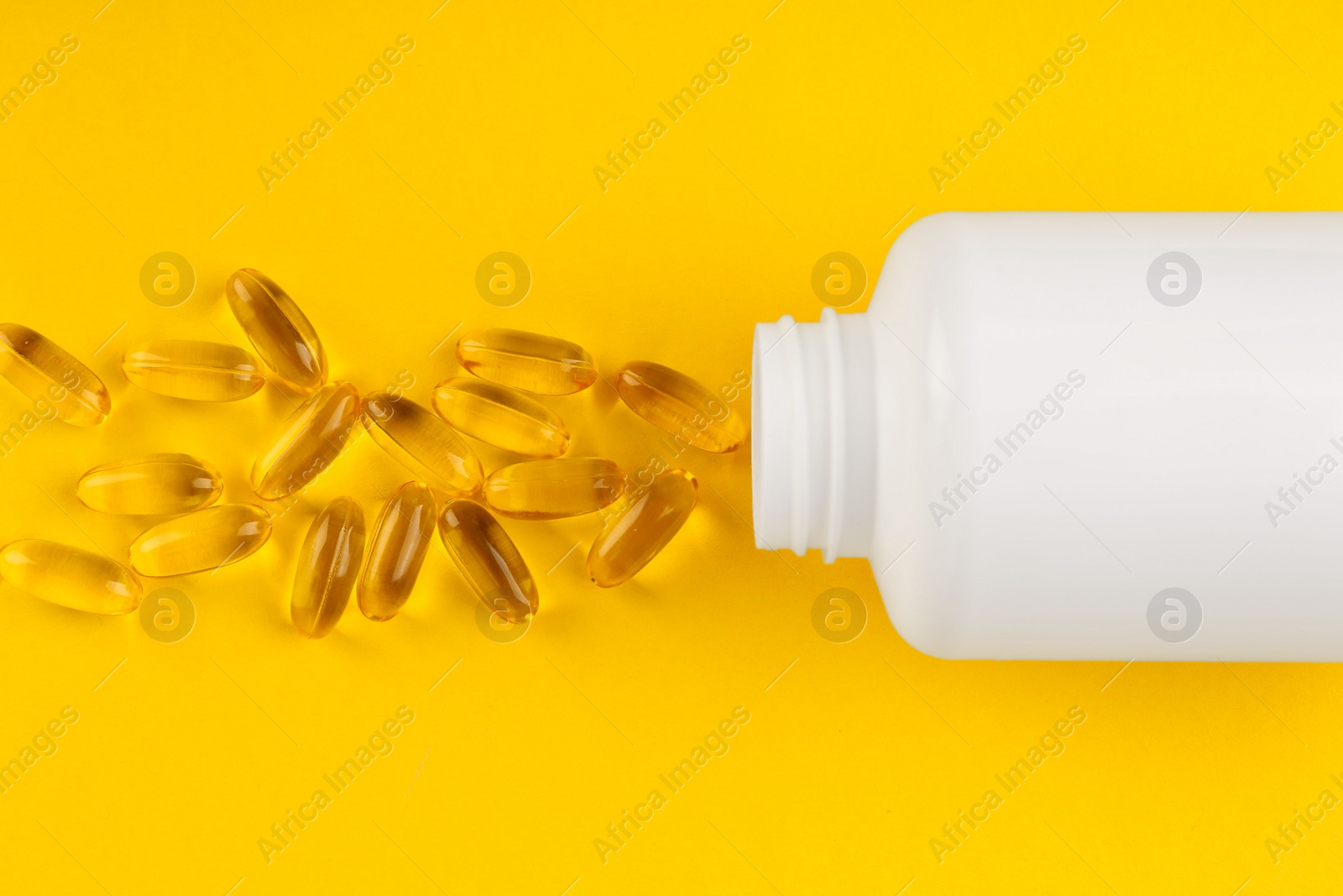 Photo of White medical bottle and vitamin capsules on yellow background, top view