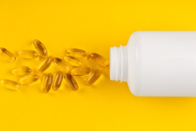 Photo of White medical bottle and vitamin capsules on yellow background, top view