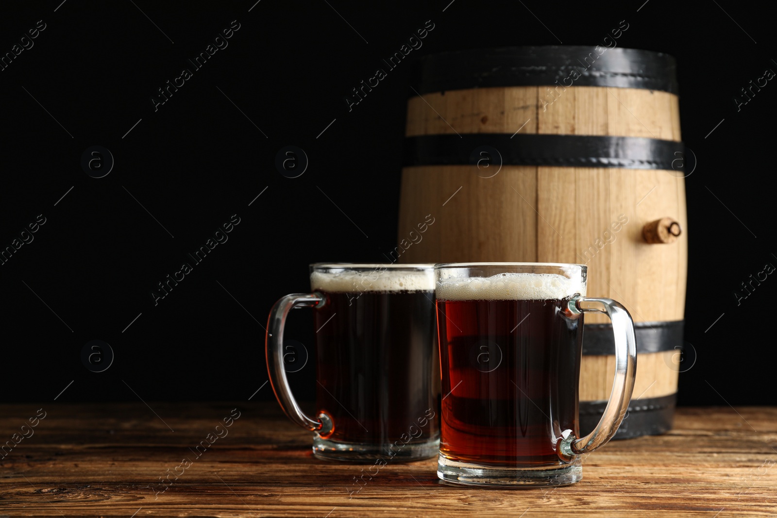 Photo of Glass mugs of delicious kvass and barrel on wooden table