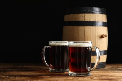 Photo of Glass mugs of delicious kvass and barrel on wooden table