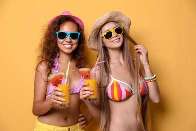 Beautiful young women in beachwear with cocktails on color background