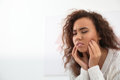 Photo of African-American woman suffering from tooth ache on light background. Space for text