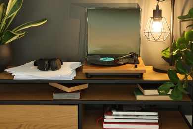 Stylish turntable with vinyl record on tv table in cozy room