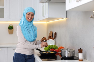 Photo of Muslim woman cooking dish in frying pan on cooktop indoors