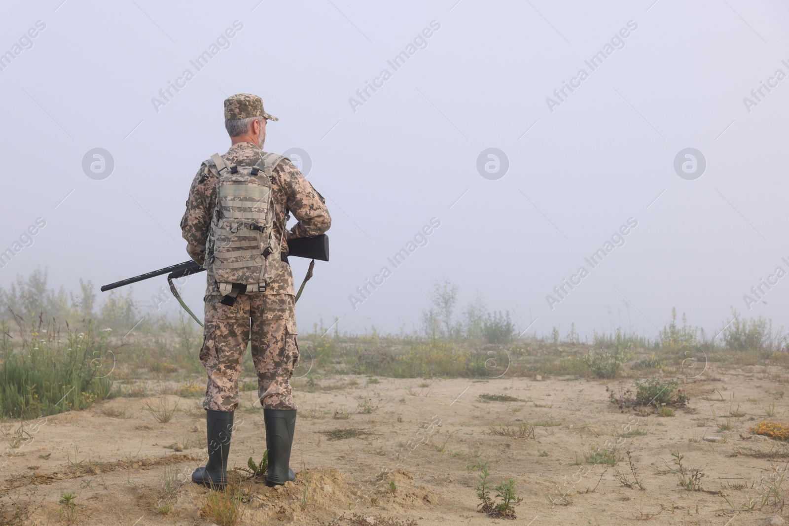 Photo of Man wearing camouflage with hunting rifle outdoors, back view. Space for text