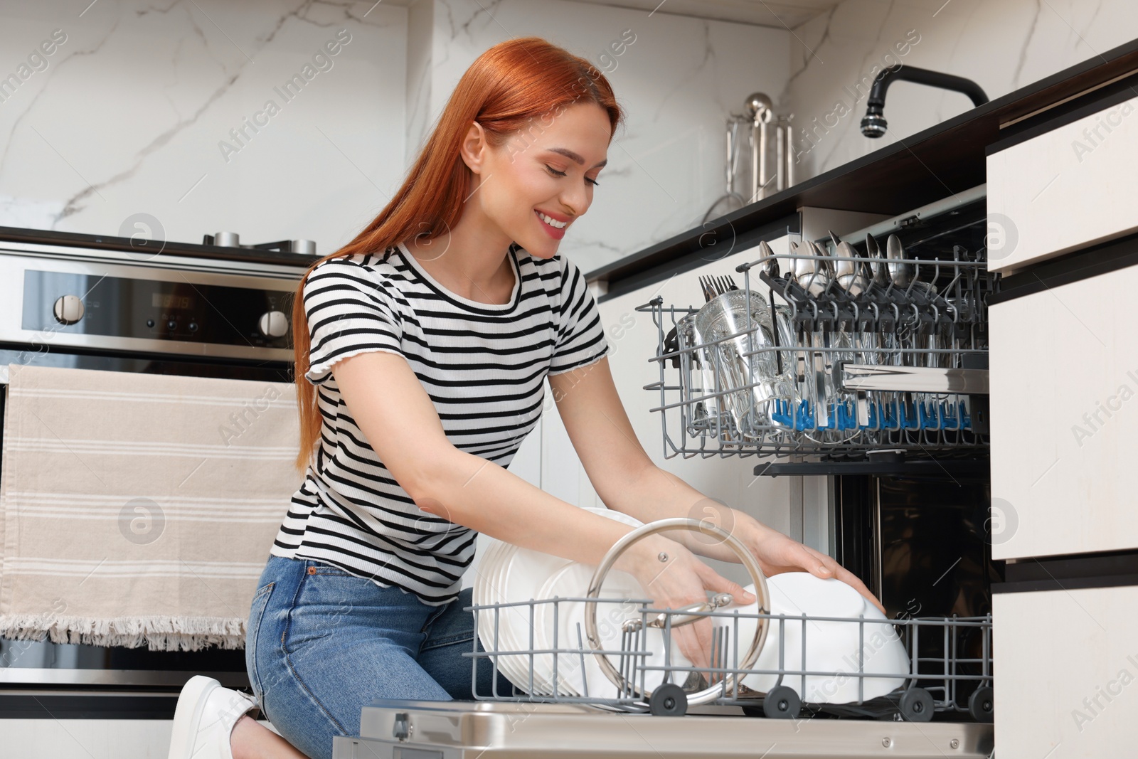 Photo of Smiling woman loading dishwasher with plates in kitchen