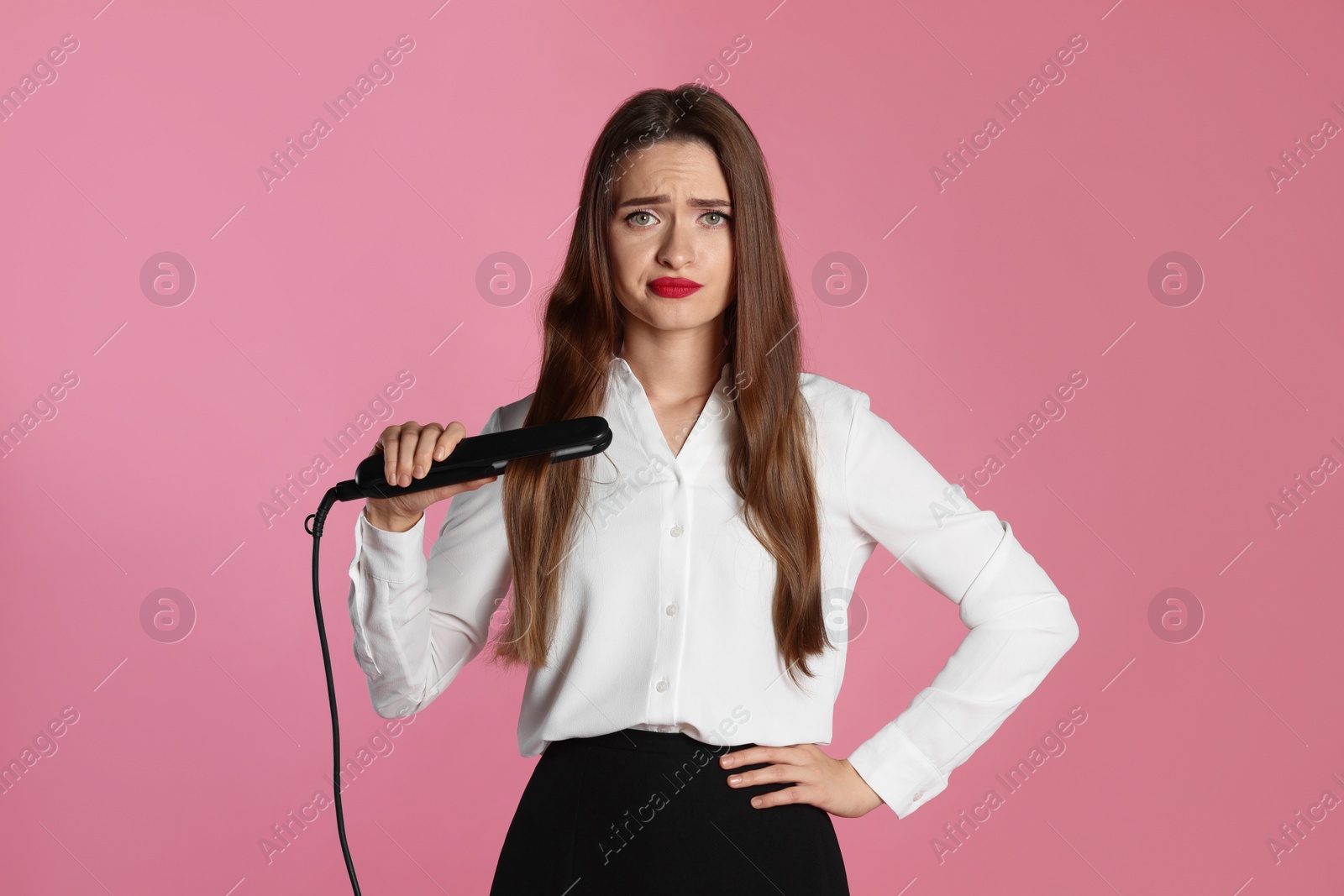 Photo of Upset young woman with flattening iron on light pink background. Hair damage