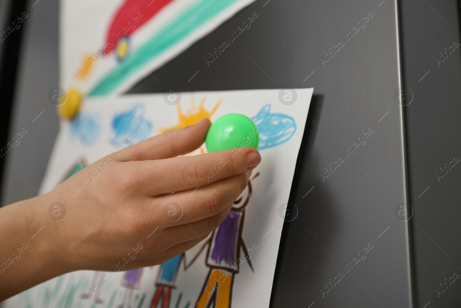 Photo of Woman putting child's drawing on refrigerator, closeup