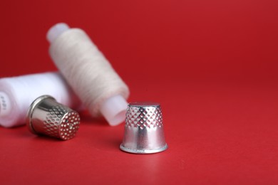 Photo of Silver thimbles and light thread on red background. Sewing accessories