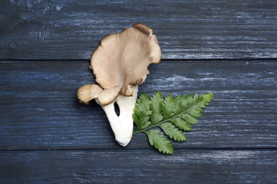 Delicious organic oyster mushrooms and leaves on wooden background, top view
