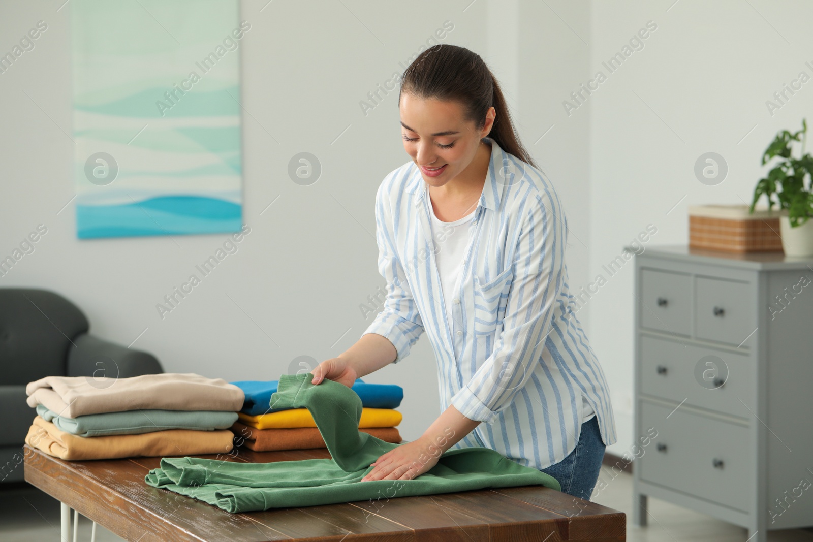 Photo of Young woman folding clothes at wooden table indoors