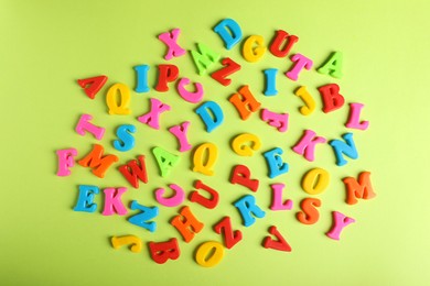 Photo of Many colorful magnetic letters on light green background, flat lay