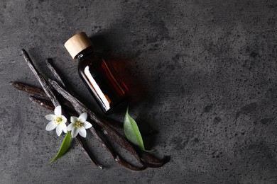 Photo of Vanilla pods, flowers, leaves and bottle with essential oil on grey textured table, flat lay. Space for text