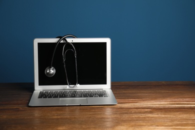 Photo of Modern laptop with stethoscope on table against color wall. Mockup for design