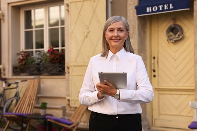 Photo of Happy business owner with tablet near her hotel outdoors, space for text